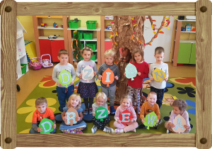 Na zdjęciu grupa dzieci. Każde dziecko trzyma literę. Litery układają się w napis DZIEŃ DRZEWA.